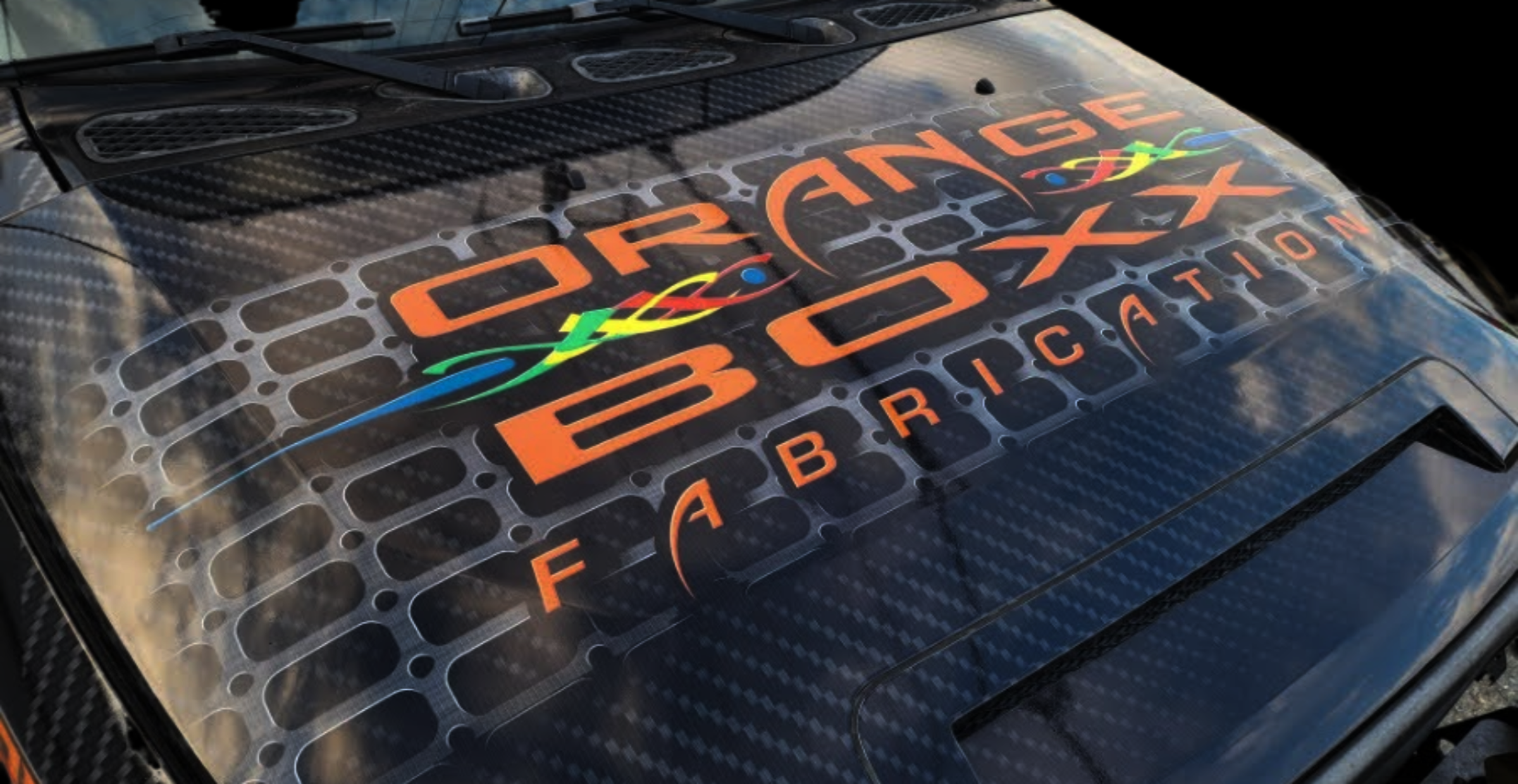 Carbon fiber surface with 'Orange Boxx Fabrication' logo
